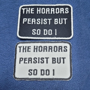 May include: Two black and white embroidered iron-on patches with the text "The Horrors Persist But So Do I".