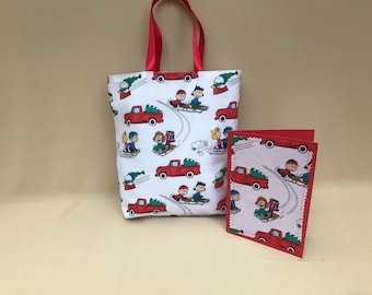 May include: A white tote bag and greeting card set featuring a repeating pattern of red trucks, children sledding, and Snoopy. The tote bag has red ribbon handles, and the card has a red border.