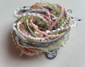 May include: A tangled ball of yarn in shades of pink, green, white, and blue. The yarn is made of different textures, including fluffy, smooth, and sparkly.
