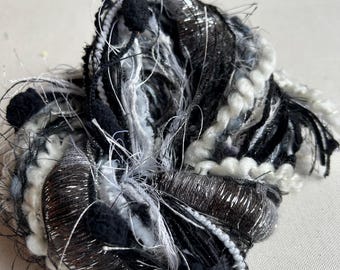 May include: A black, white, and silver yarn with fluffy texture and black pom-poms.