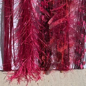 May include: A collection of decorative yarn strands in various shades of pink, magenta, and deep red. The assortment includes smooth, thin threads, fuzzy eyelash-style textured fibers, and metallic ribbons arranged vertically on a white card.