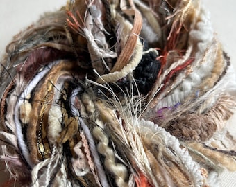 May include: A ball of mixed fiber yarn in various neutral tones, including beige, brown, and cream, with accents of black, orange, and gold. The yarn appears to be a blend of textures, with some sections appearing fuzzy and others smooth.