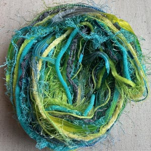 May include: A vibrant ball of yarn in shades of teal, lime green, and yellow. The yarn has a textured appearance with various strands and textures, creating a visually interesting and tactile appeal. The yarn is likely used for crafting projects.