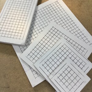 Peut inclure: Cinq planches blanches quadrillées de différentes tailles, empilées les unes sur les autres. Les planches sont faites d'un matériau épais et résistant et ont une surface lisse et blanche.