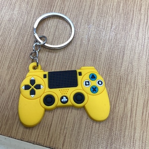 以下が含まれることがあります： 黒いボタンと銀色のキーリングが付いた、黄色のプラスチック製のPlayStationコントローラーキーホルダーです。