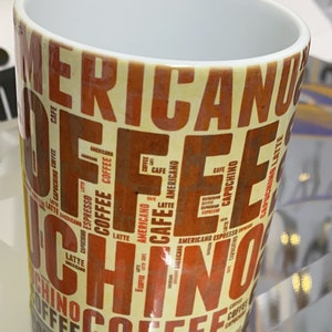 May include: A white ceramic mug with a yellow and orange design. The mug is covered in the words "Coffee", "Americano", "Cappuccino", "Latte", and "Espresso" in a repeating pattern.