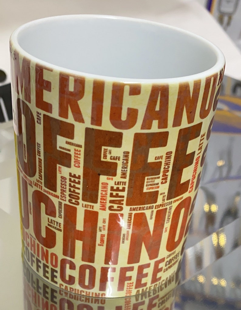May include: A white ceramic mug with a yellow and orange design. The mug is covered in the words "Coffee", "Americano", "Cappuccino", "Latte", and "Espresso" in a repeating pattern.