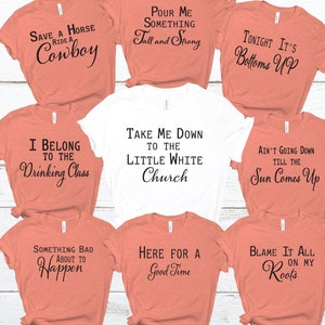 May include: Nine different t-shirts with various sayings printed on them. The shirts are in two colors: peach and white. The sayings include: "Save a Horse Ride a Cowboy", "Pour Me Something Tall and Strong", "Tonight It's Bottoms Up", "I Belong to the Drinking Class", "Take Me Down to the Little White Church", "Ain't Going Down Till the Sun Comes Up", "Something Bad About to Happen", "Here for a Good Time", and "Blame It All on My Roots".