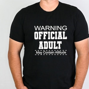 May include: Black t-shirt with white text that reads "WARNING OFFICIAL ADULT May Contain Attitude".