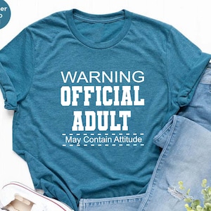 May include: A teal blue t-shirt with the text "WARNING OFFICIAL ADULT May Contain Attitude" in white.