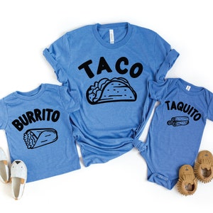 May include: Three blue t-shirts with a taco, burrito, and taquito design. The shirts are for a family of three.