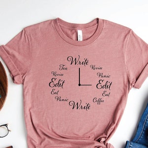 May include: A pink t-shirt with a clock design featuring the words "Write, Revise, Edit, Eat, Panic, Tea, Coffee".