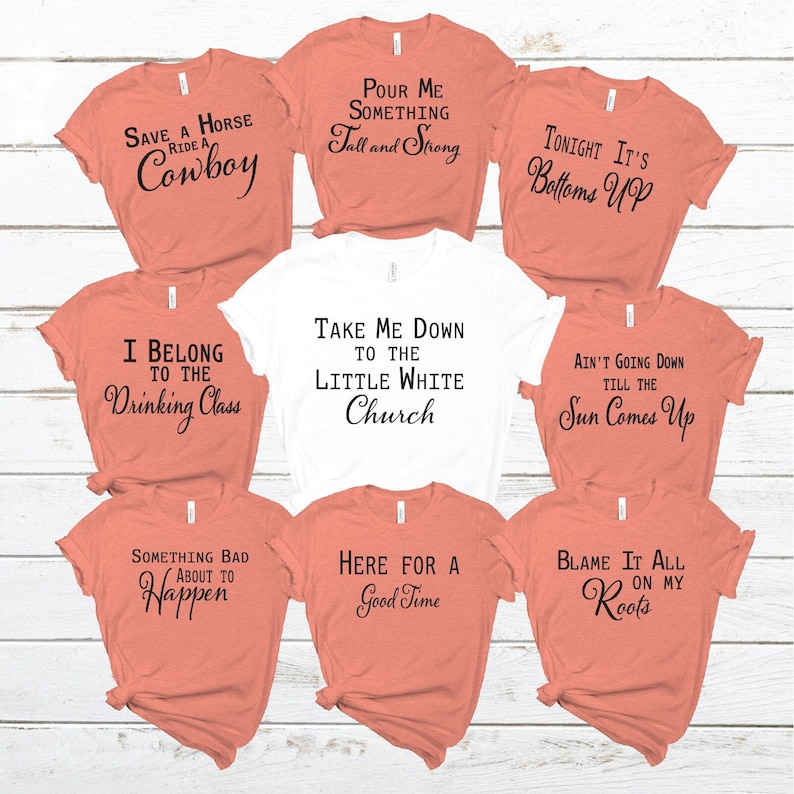 May include: Nine different t-shirts with various sayings printed on them. The shirts are in two colors: peach and white. The sayings include: "Save a Horse Ride a Cowboy", "Pour Me Something Tall and Strong", "Tonight It's Bottoms Up", "I Belong to the Drinking Class", "Take Me Down to the Little White Church", "Ain't Going Down Till the Sun Comes Up", "Something Bad About to Happen", "Here for a Good Time", and "Blame It All on My Roots".