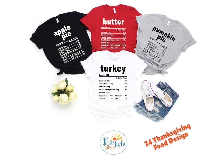 May include: Four white t-shirts with black text, each featuring a different Thanksgiving food item: apple pie, butter, pumpkin pie, and turkey. The shirts are laid out on a white surface with a bouquet of white flowers and a pair of white sneakers. The text on the shirts is formatted to look like a nutrition label.