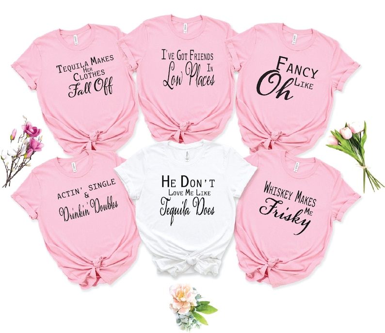 May include: Six pink and white t-shirts with funny sayings about alcohol. The sayings include "Tequila Makes Her Clothes Fall Off", "I've Got Friends In Low Places", "Fancy Oh Like", "Actin' Single & Drinkin' Doubles", "He Don't Love Me Like Tequila Does", and "Whiskey Makes Me Frisky".