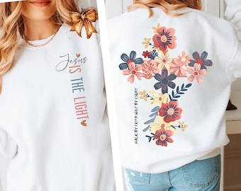 May include: White sweatshirt with the text "Jesus is the Light" in a vertical design. The back of the sweatshirt features a floral cross design with various colors. The phrase "Walk by faith not by sight" is printed vertically.