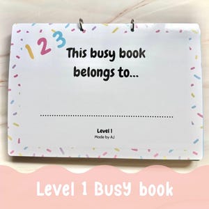 May include: A rectangular spiral-bound busy book with a white cover featuring a colourful sprinkle border. The text reads "1 2 3", "This busy book belongs to...", a dotted line for a name, "Level 1", and "Made by AJ" in black lettering.