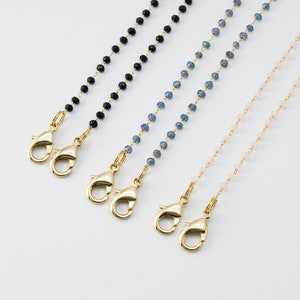 May include: Four beaded chains with gold-coloured clasps. The chains feature black, blue, and pink beads. The clasps are open and ready to be attached. The background is white.