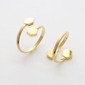 May include: Two gold-colored, open-ended rings. Each ring features a hexagonal accent on each end of the band. The rings are displayed on a white background, showcasing their minimalist design and metallic sheen.