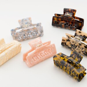 May include: Six different hair clips in various colors and patterns. The clips are made of plastic and have a tortoise shell, pink, cream, and blue and white marbled design.