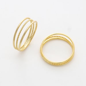 May include: Two gold rings with a twisted design. The ring on the left has three bands, while the ring on the right has two bands.