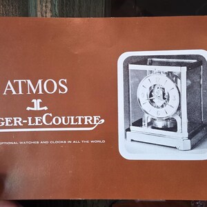 May include: A brochure with the text "ATMOS JAEGER-LECOULTRE" in white on a brown background. The brochure features a black and white image of an Atmos clock. The text at the bottom reads "THE MOST EXCEPTIONAL WATCHES AND CLOCKS IN ALL THE WORLD."
