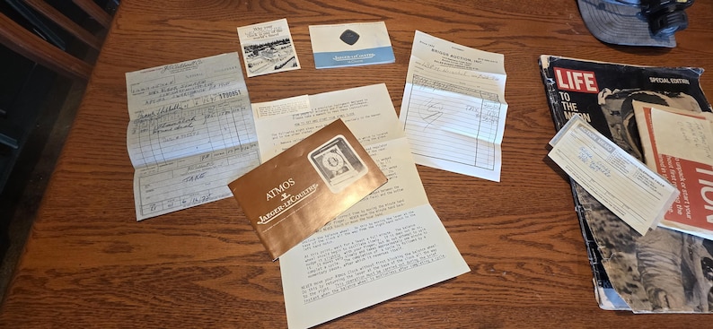 May include: A collection of vintage ephemera, including receipts, brochures, and a magazine. The items are arranged on a wooden surface. A brochure for "The Broadmoor" is visible, along with a "LIFE" magazine with the headline "LIFE TO THE MOON".
