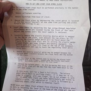 May include: A printed instruction sheet for an Atmos clock, detailing how to set and start the clock. The text is in black font on a white background. The sheet includes a warning about handling the clock.