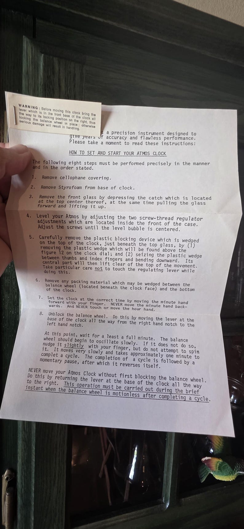 May include: A printed instruction sheet for an Atmos clock, detailing how to set and start the clock. The text is in black font on a white background. The sheet includes a warning about handling the clock.