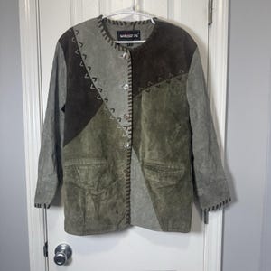 May include: A patchwork suede jacket in shades of green, gray, and brown. The jacket features a round collar, button closure, and two front pockets. Decorative stitching and the brand name "Monsini" are visible.