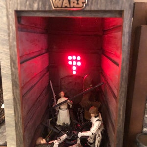 Könnte beinhalten: Ein Star Wars-Diorama in einer Holzkiste mit Miniaturfiguren von Charakteren. Die Szene zeigt Prinzessin Leia, Chewbacca und Sturmtruppen. Das Star Wars-Logo ist oben zu sehen.
