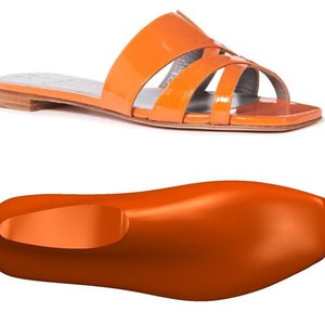 May include: Orange leather sandals with a criss-cross strap design. The sandals have a flat sole and a slightly squared toe.