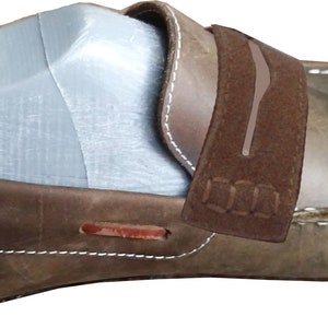 Peut inclure: Mocassin en cuir marron avec une bride en daim et des d&eacute;tails de couture blanche. La bride porte l'inscription "D.N.A.".