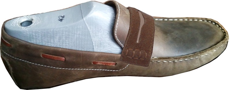 Peut inclure: Mocassin en cuir marron avec une bride en daim et des d&eacute;tails de couture blanche. La bride porte l'inscription "D.N.A.".