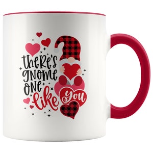 May include: White ceramic coffee mug with a red rim and handle. The mug features a red and black plaid gnome holding a red heart with the text "There's gnome one like you".