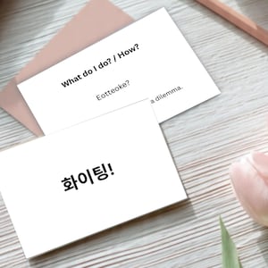 May include: Two white cards with text, one reading "What do I do? / How?" and "Eotteoke?", the other with Korean characters. A pink envelope, a pencil, and pink tulips are also visible.