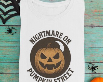 May include: White t-shirt with a round graphic featuring a jack-o'-lantern and the text "NIGHTMARE ON PUMPKIN STREET". The shirt is surrounded by Halloween decorations, including spiders and pumpkins.