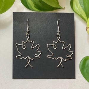 May include: A pair of silver wire earrings shaped like maple leaves. The earrings are delicate and have a simple design.