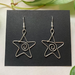 May include: A pair of silver wire earrings shaped like stars with a spiral design in the center.