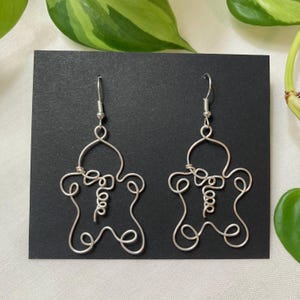 May include: A pair of silver wire earrings shaped like a person with the word "love" written on the body.