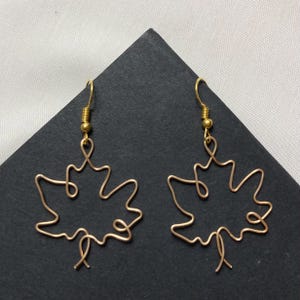 May include: A pair of gold wire earrings shaped like maple leaves. The earrings are delicate and have a simple design.