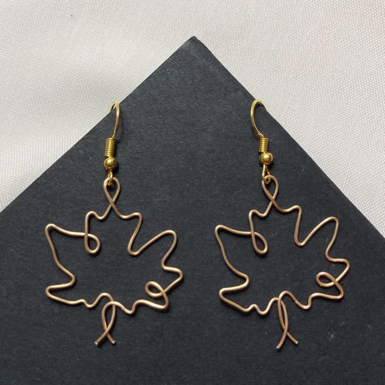 May include: A pair of gold wire earrings shaped like maple leaves. The earrings are delicate and have a simple design.