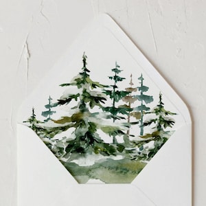 May include: A white envelope with a watercolor painting of evergreen trees inside. The trees are green and brown, with a hint of snow. The envelope is on a white textured surface.