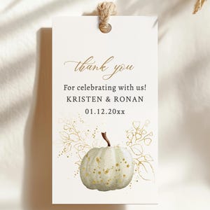 Peut inclure: Etiquette de remerciement blanche avec des paillettes dorées et une citrouille blanche avec des paillettes dorées. L'étiquette indique "merci" et "Pour avoir célébré avec nous ! KRISTEN & RONAN 01.12.20xx". L'étiquette est munie d'une ficelle brune attachée au sommet.