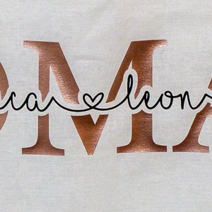 Könnte beinhalten: Roségoldene metallische Buchstaben, die "OMA" buchstabieren, mit den Namen "Luca" und "Leon", die in Kursivschrift mit einem Herzsymbol dazwischen geschrieben sind.