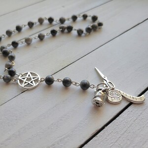 May include: A silver necklace with a pentagram charm and a charm with a spool of thread, scissors, and a measuring tape. The necklace is made of gray beads.