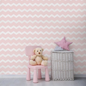 Puede incluir: Una silla rosa para niños con un oso de peluche sentado en ella. Una cesta de almacenamiento de mimbre blanca con una almohada en forma de estrella rosa en la parte superior se encuentra junto a la silla. La pared detrás de la silla y la cesta está cubierta con un papel tapiz de patrón de chevron rosa y blanco.