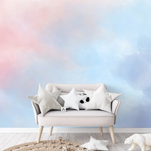 Può includere: Un divano bianco con tre cuscini, due bianchi e uno con un disegno di panda nero, si trova di fronte a un muro con un design di nuvole ad acquerello rosa e blu. Il divano ha una lettera "A" sul sedile.