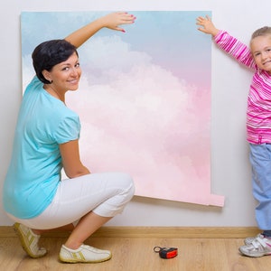 May include: A woman and a girl are putting up a large pink and blue watercolor wall mural. The mural features a cloudy sky design.