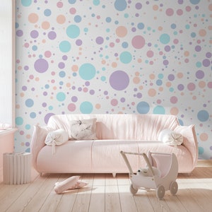 Puede incluir: Un sofá rosa con almohadas blancas se encuentra frente a una pared con un patrón de lunares pastel. La pared está cubierta de círculos de diferentes colores pastel, azul claro, rosa y melocotón.